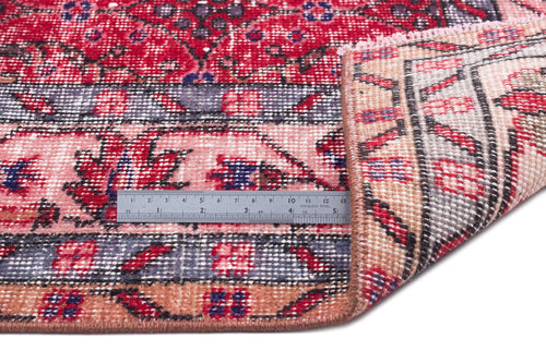 Load image 1 in gallery view. Red, pink, and blue distressed Persian-style rug with a floral pattern, shown with a metal ruler for scale.