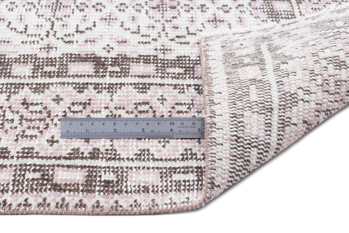 Pink and brown geometric patterned rug with a folded corner and a metal ruler for scale on a white background.