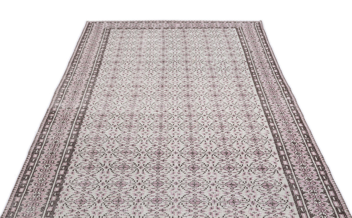 Cream and mauve area rug with a repeating geometric medallion pattern and a wide, detailed border.