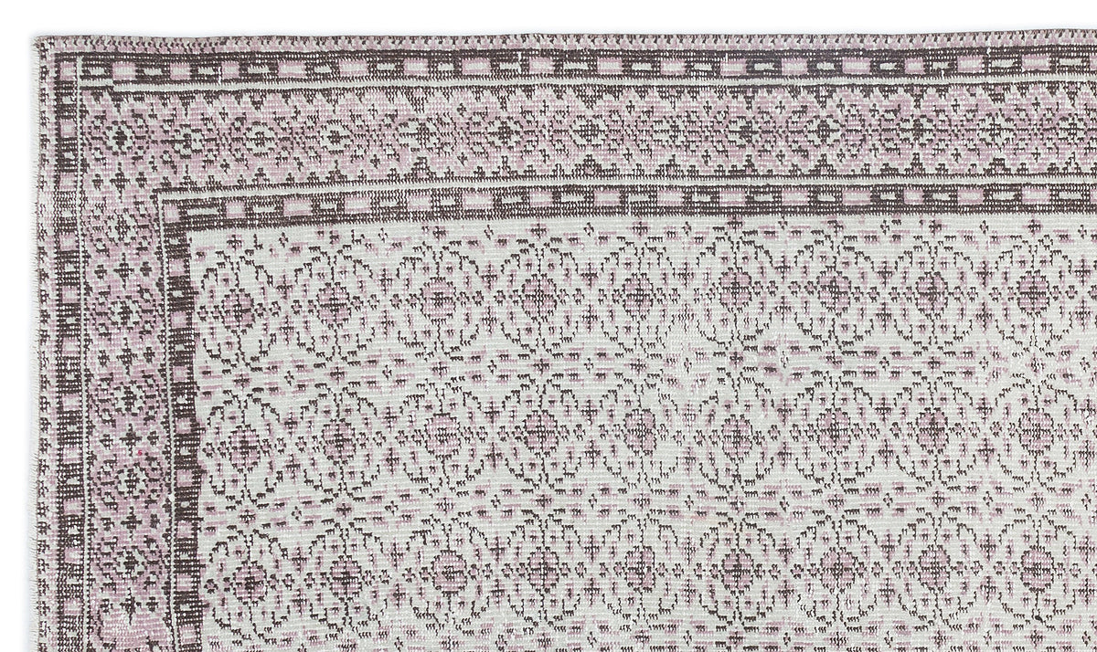 Dusty pink and cream rug with a traditional geometric border and repeating floral medallion pattern.