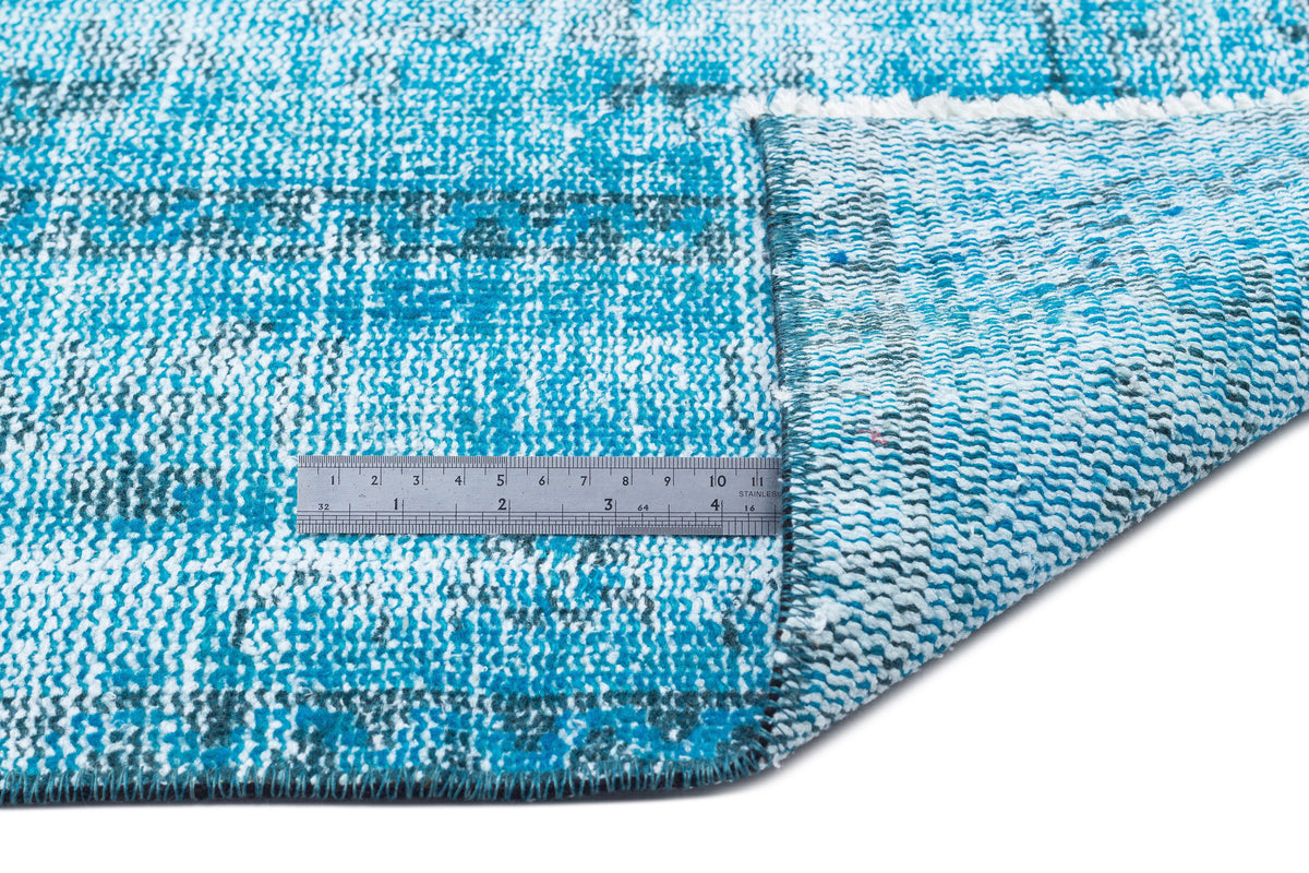 Distressed turquoise and white patterned rug with a folded corner and a metal ruler for scale.
