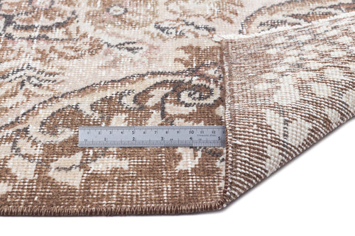Load image 1 in gallery view. Brown and cream distressed floral medallion rug with a folded corner and a metal ruler for scale.