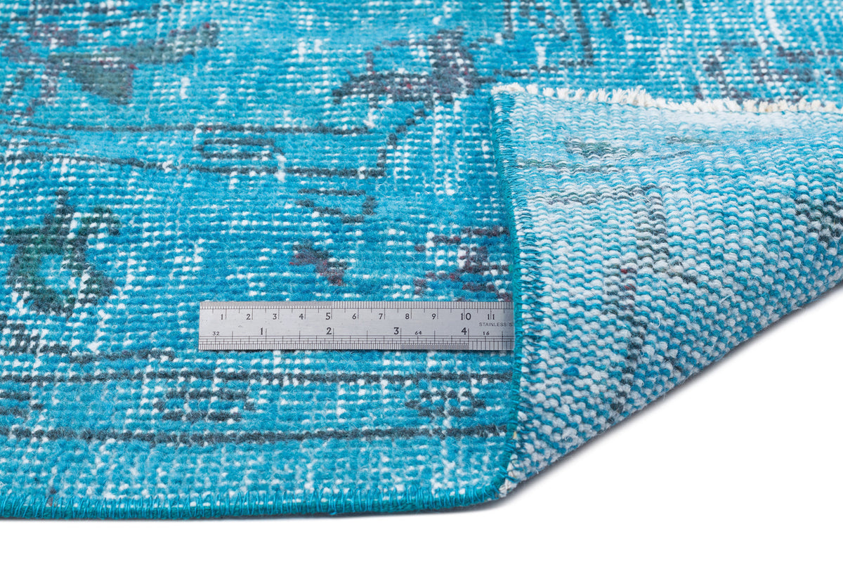 Bright blue distressed rug with a faded geometric pattern, shown with a metal ruler for scale on a white background.