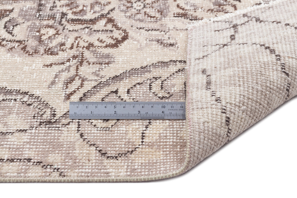Beige and brown floral patterned rug with a corner folded over to show the woven backing and a metal ruler for scale.