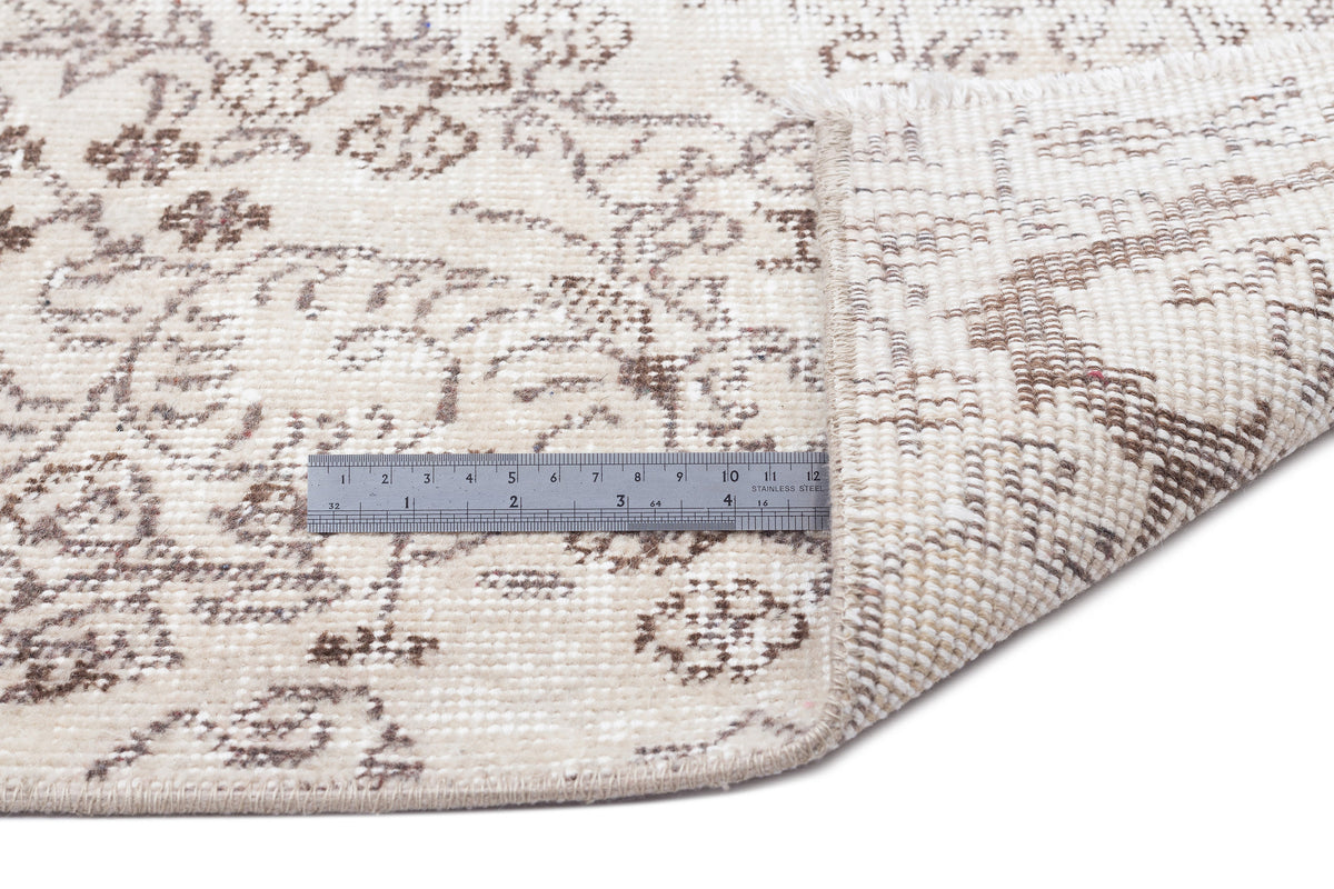 Beige and brown traditional floral pattern rug with a corner folded over, showing the woven backing and a metal ruler.