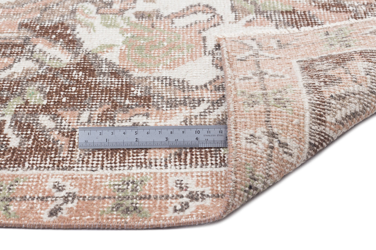 Distressed brown, cream, and sage green vintage-style rug with a floral medallion pattern and a metal ruler for scale.