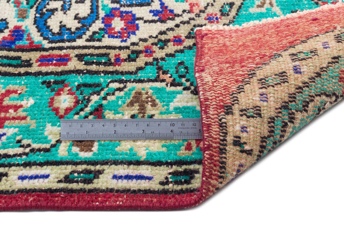 Vintage-style rug with a floral medallion pattern in teal, red, and beige, shown with a metal ruler for scale.