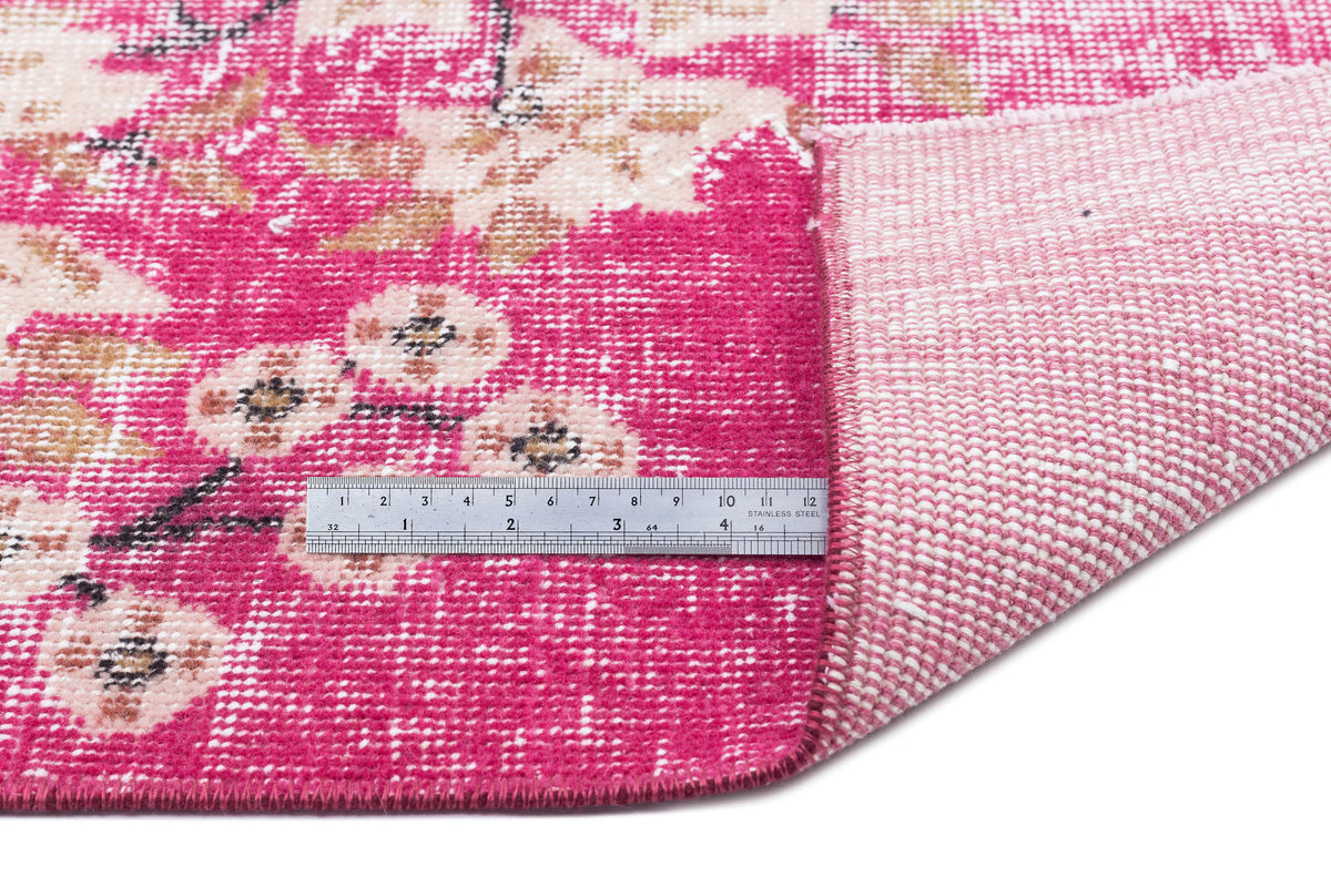 Hot pink and cream floral rug with a distressed texture, shown with a metal ruler for scale on a white background.