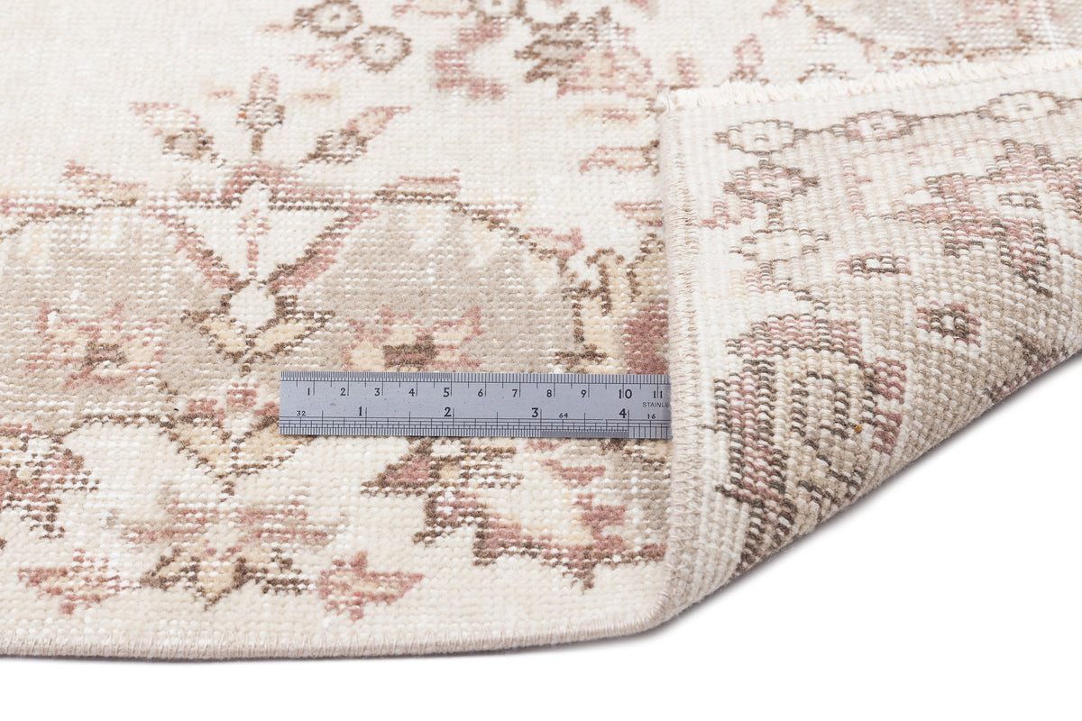 Cream and beige rug with a faded floral medallion pattern, shown with a metal ruler for scale on a white background.