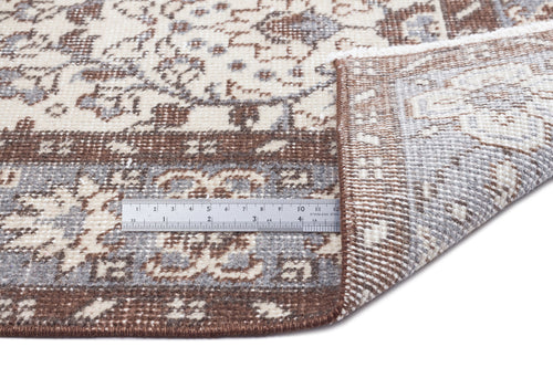 Load image 1 in gallery view. Brown, grey, and cream traditional floral rug with a folded corner and a metal ruler for scale on a white background.