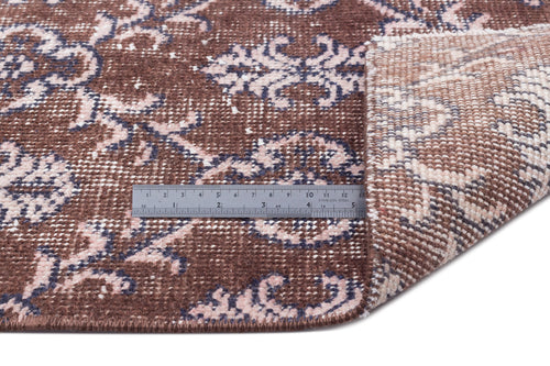 Load image 1 in gallery view. Brown rug with a faded floral pattern in pink and dark blue, shown with a metal ruler for scale.