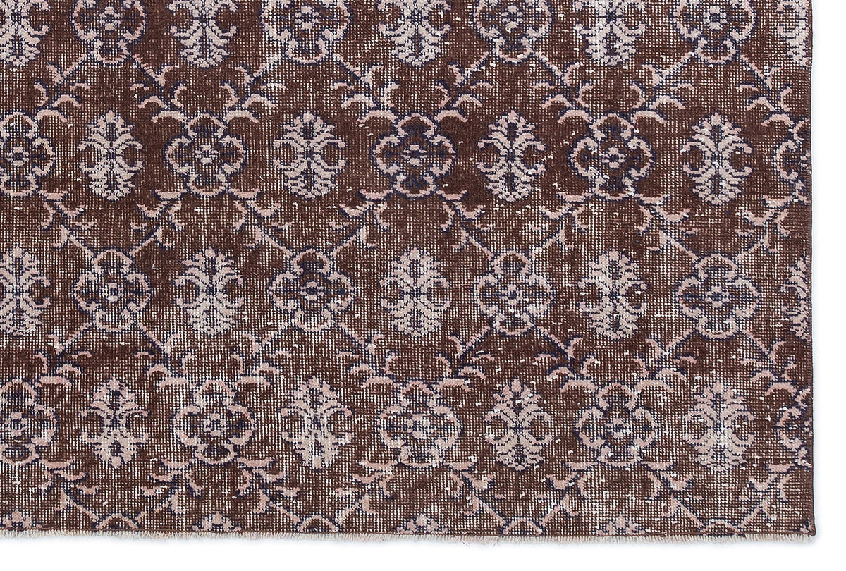 Dark brown rug with a repeating light pink and cream floral medallion pattern in a distressed, vintage style.