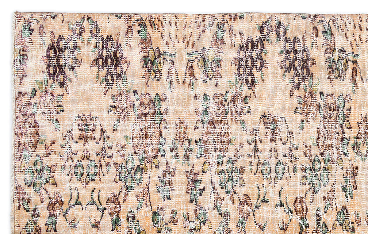Peach-toned rug with a distressed, repeating floral medallion pattern in muted brown, green, and cream.