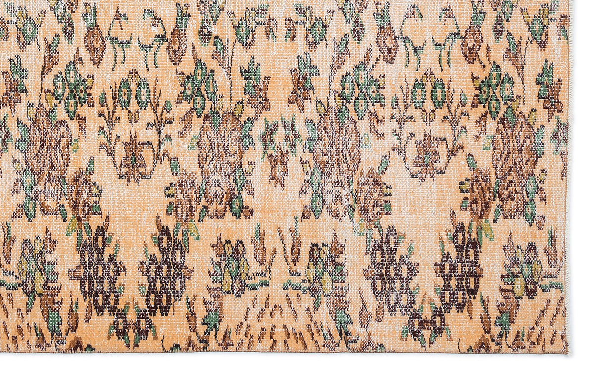 Peach-toned rug with a distressed floral pattern in shades of brown, green, and cream.