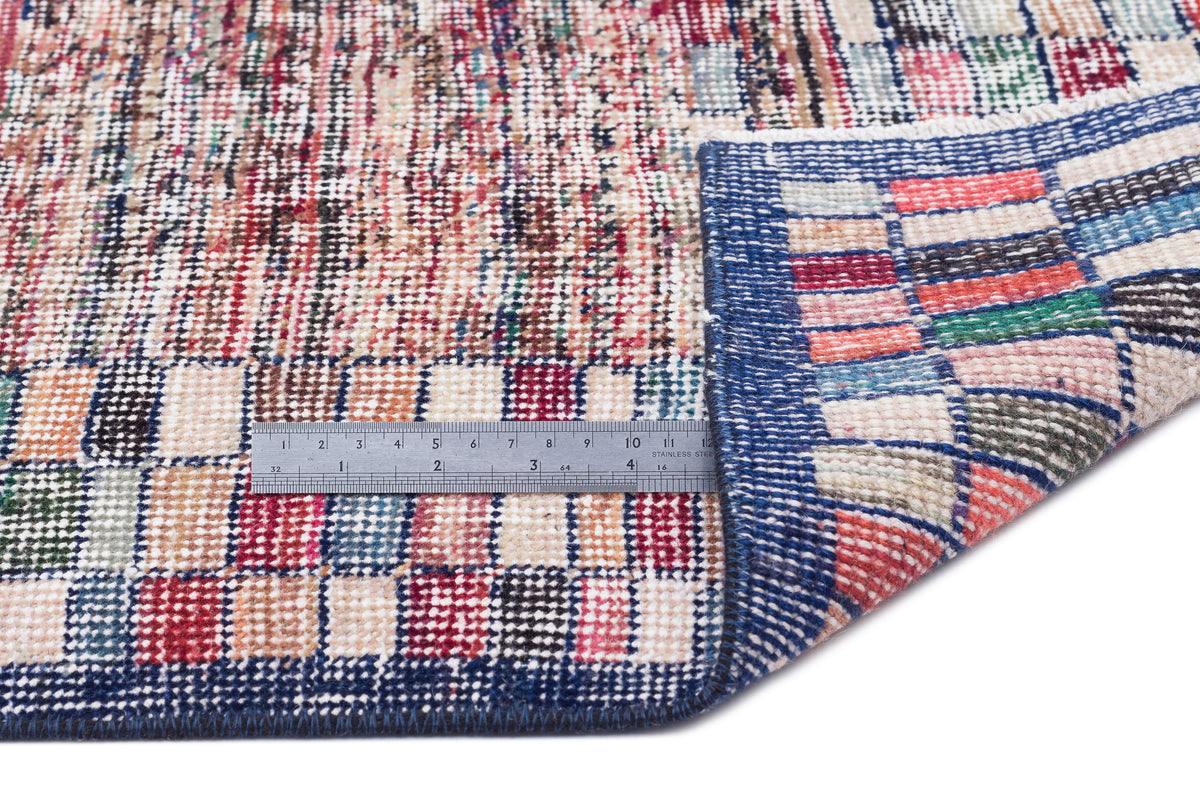 Multicolor patchwork rug with a grid pattern and blue border, shown with a metal ruler for scale on a white background.