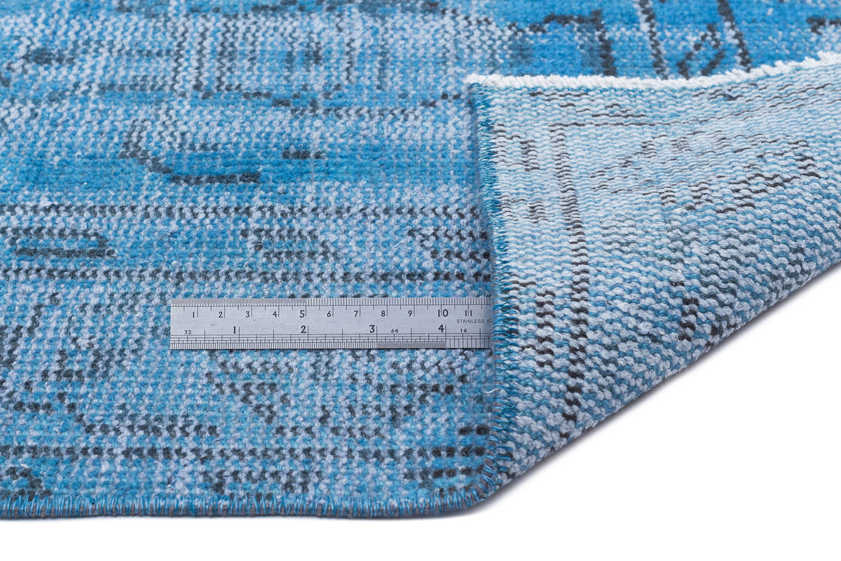 Blue and white distressed patterned rug with a folded corner and a stainless steel ruler for scale.