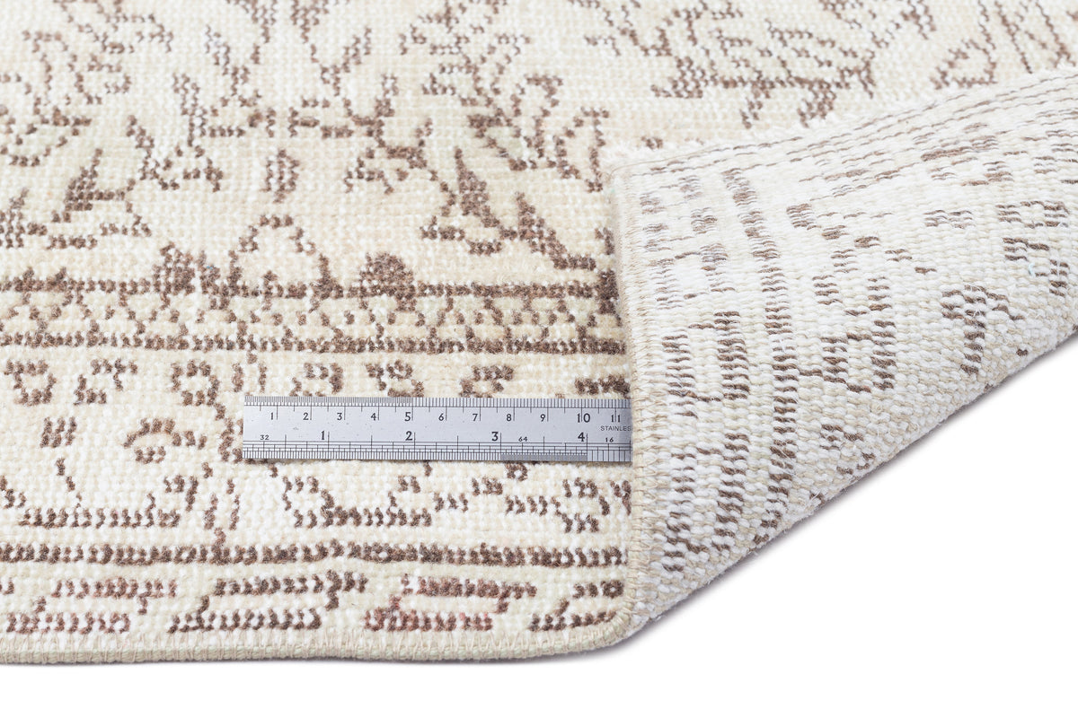 Cream and beige rug with a distressed floral pattern, shown with a metal ruler for scale on a white background.