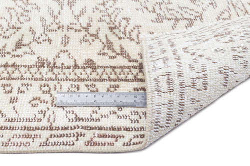Load image 1 in gallery view. Cream and beige rug with a distressed floral pattern, shown with a metal ruler for scale on a white background.