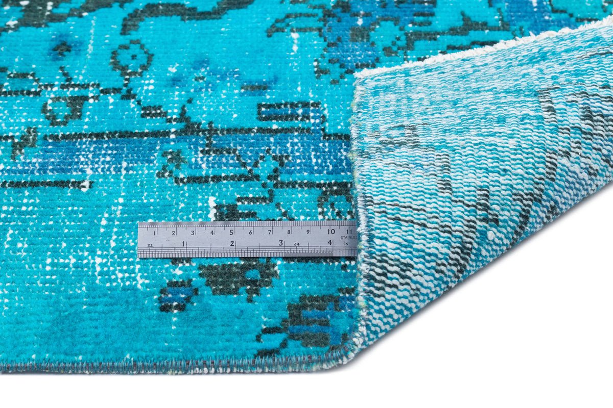 Bright turquoise and dark blue distressed traditional rug with a metal ruler showing scale, on a white background.