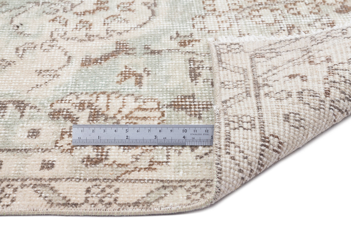 Beige and sage green distressed traditional rug with a floral medallion pattern, shown with a metal ruler for scale.