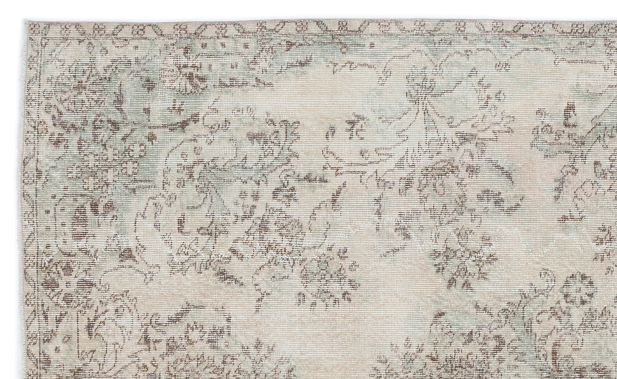 Beige and sage green rug with a distressed, faded floral medallion pattern on a white background.