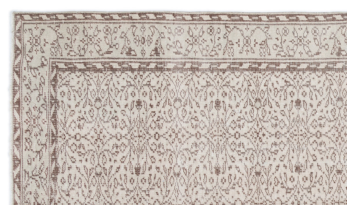 Beige and brown flatweave rug with a traditional floral vine pattern and geometric border on a white background.