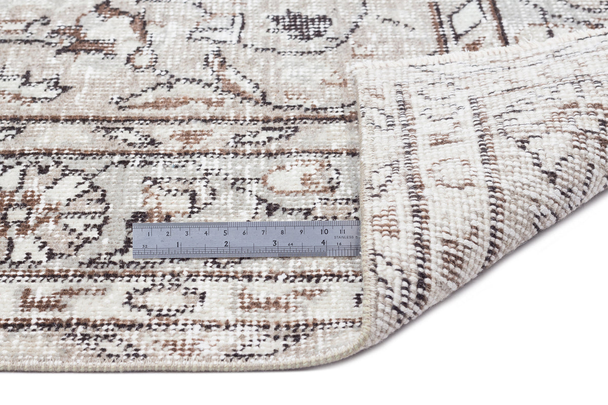 Beige and brown distressed traditional rug with a folded corner and a metal ruler for scale on a white background.