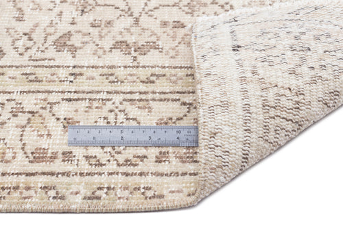 Load image 1 in gallery view. Beige and taupe distressed traditional rug with a folded corner and a metal ruler for scale on a white background.