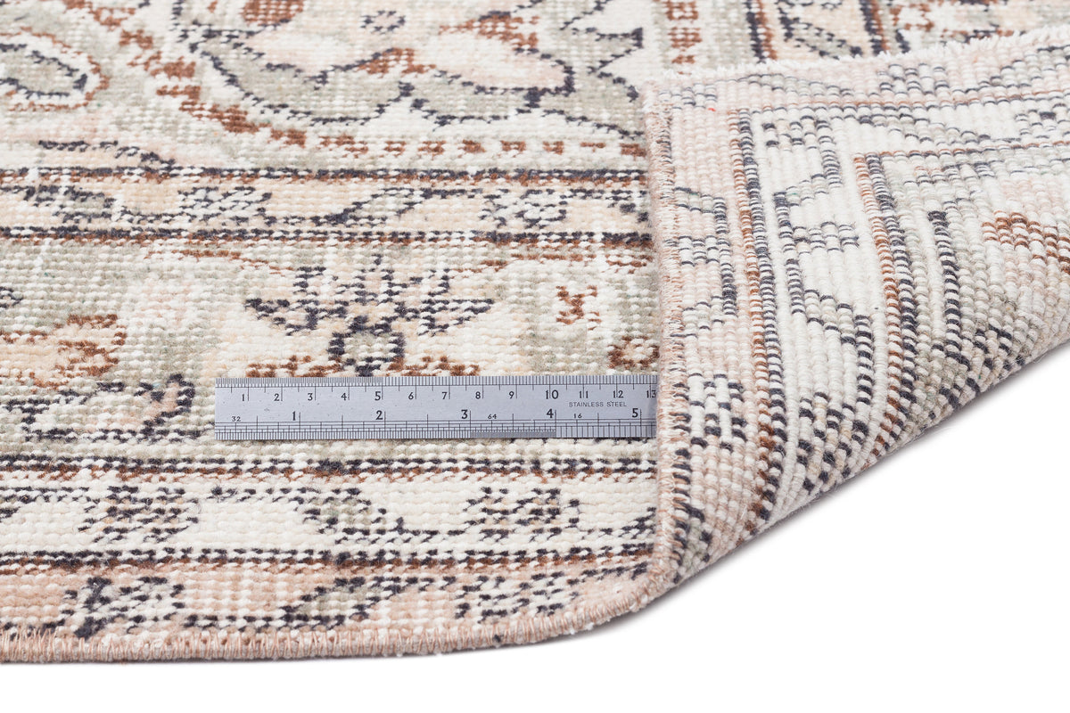 Cream, sage, and rust-toned rug with a distressed traditional pattern, shown with a metal ruler for scale.