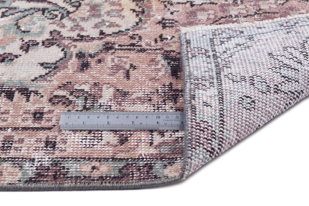 Distressed floral medallion rug in dusty rose, sage, and cream with a corner folded back to show the woven backing.