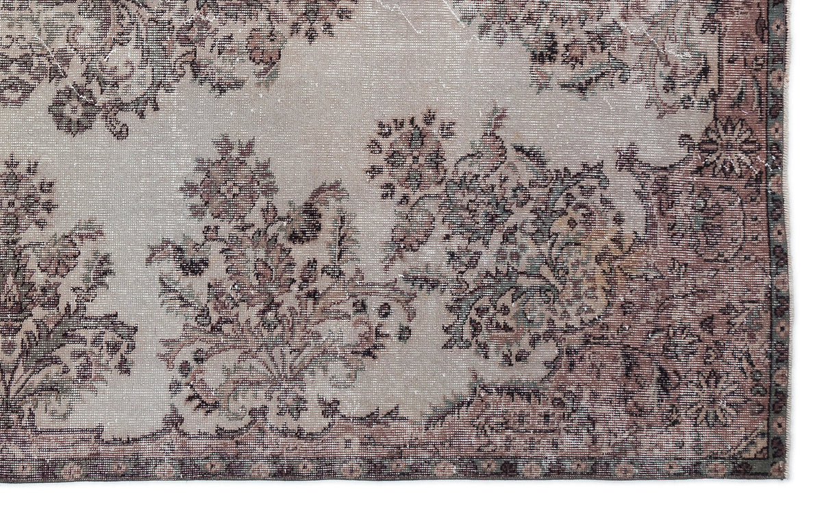 Distressed beige rug with a faded floral medallion pattern in muted brown, charcoal, and sage green tones.