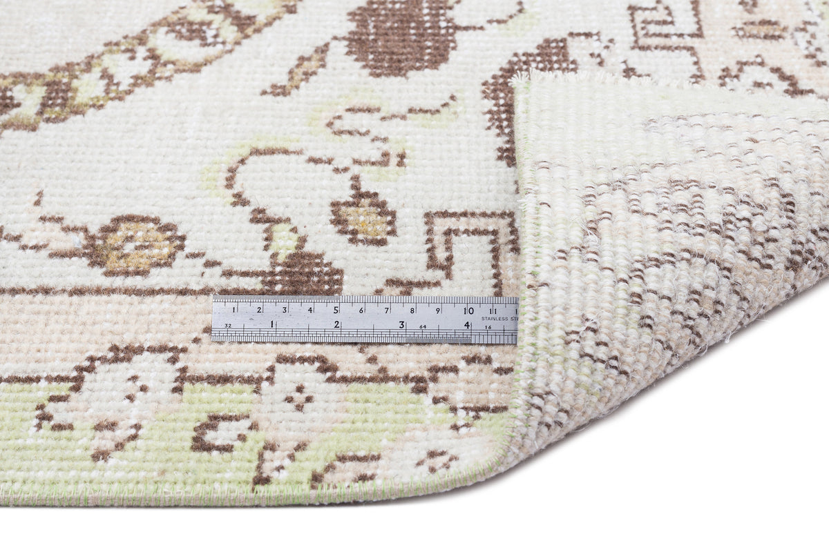 Cream, brown, and pale green rug with a traditional floral pattern, shown with a metal ruler for scale.