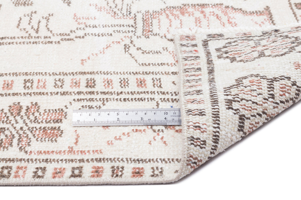 Cream rug with brown and terracotta geometric tribal patterns, shown with a metal ruler for scale.