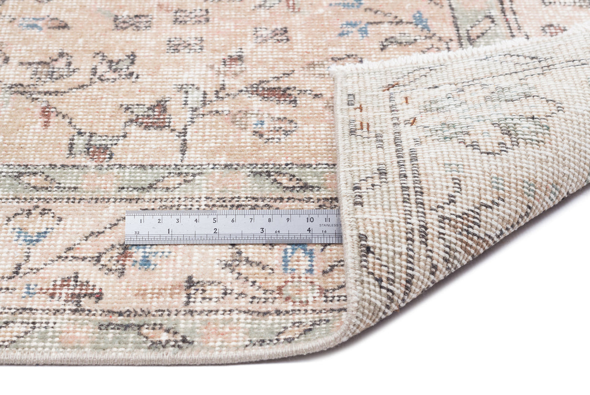 Beige and sage green vintage-style rug with a floral pattern, showing the woven backing and a metal ruler for scale.