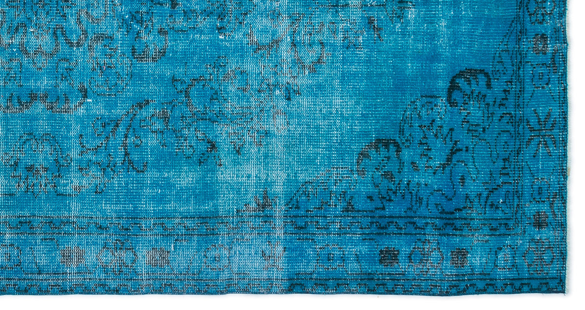 Bright blue rug with a distressed black floral medallion pattern and a geometric border.