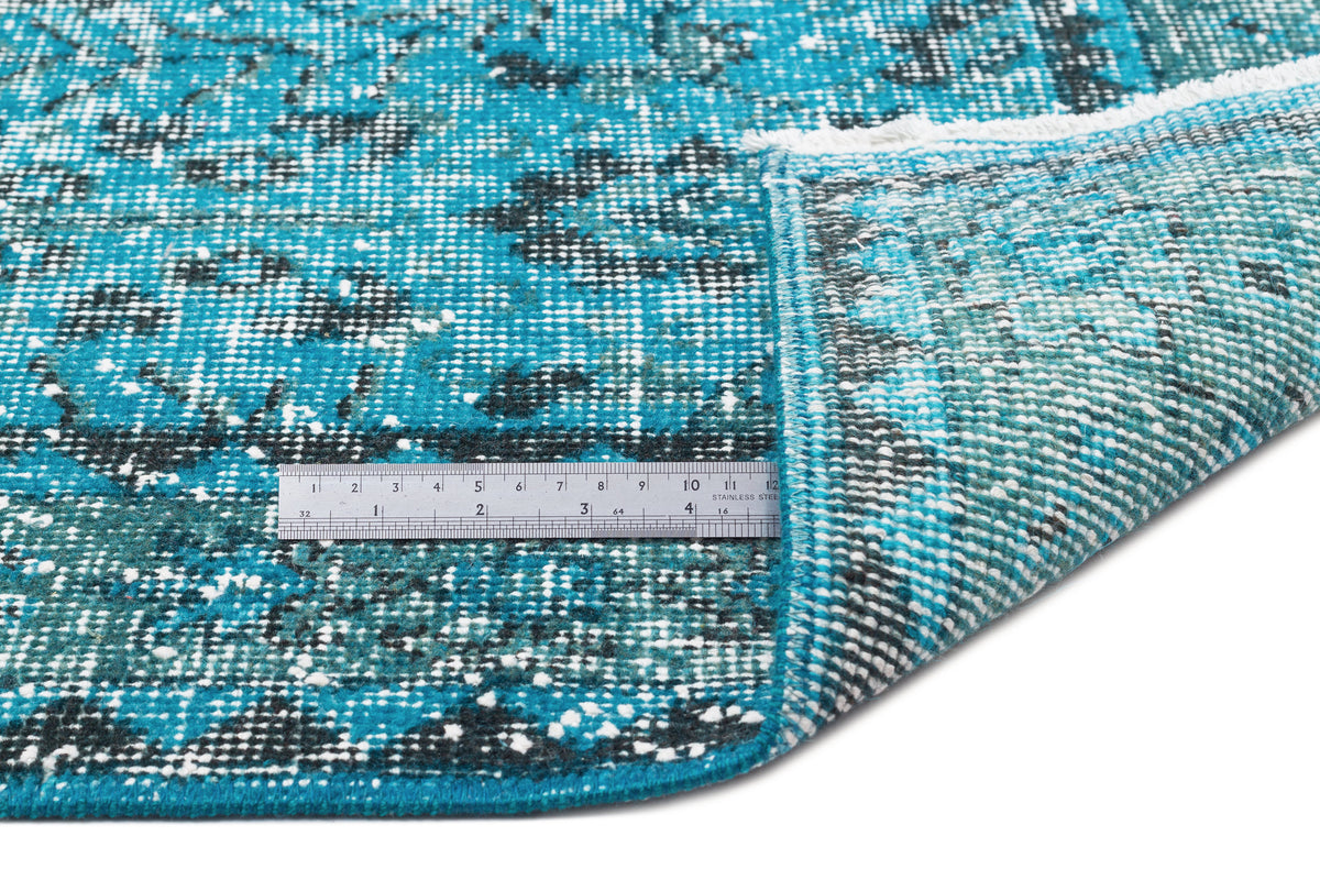 Turquoise and black distressed medallion rug with white fringe, shown with a metal ruler for scale on a white background.