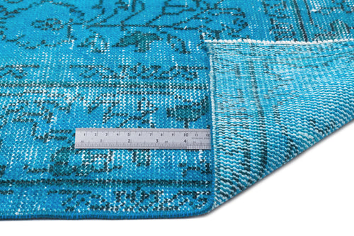 Load image 1 in gallery view. Bright blue distressed rug with a dark floral pattern, shown folded to reveal the woven backing and a metal ruler.