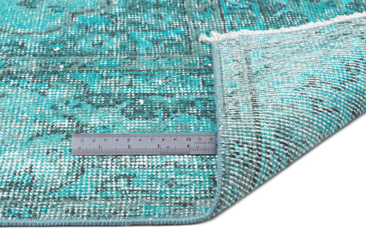 Distressed turquoise and charcoal traditional rug with a white fringe, shown with a metal ruler for scale.