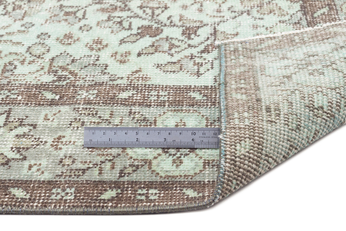 Mint green and brown distressed floral rug with a folded corner and a metal ruler for scale.