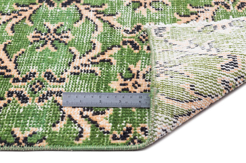 Load image 1 in gallery view. Green, black, and beige floral patterned rug with a folded corner and a metal ruler for scale on a white background.