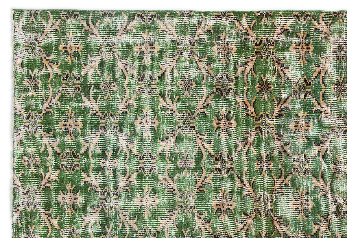Green rug with a distressed, repeating beige and black floral medallion pattern on a white background.
