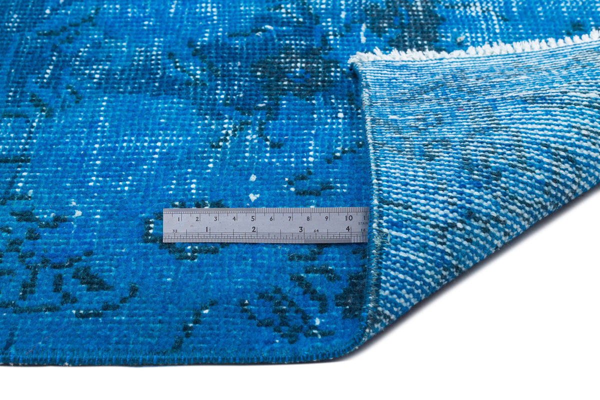 Bright blue distressed rug with a dark blue floral pattern and white fringe, shown with a metal ruler for scale.