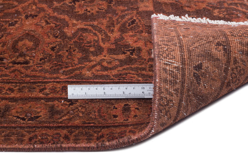 Load image 1 in gallery view. Rust and dark brown traditional rug with a floral medallion pattern, shown with a corner folded and a metal ruler.