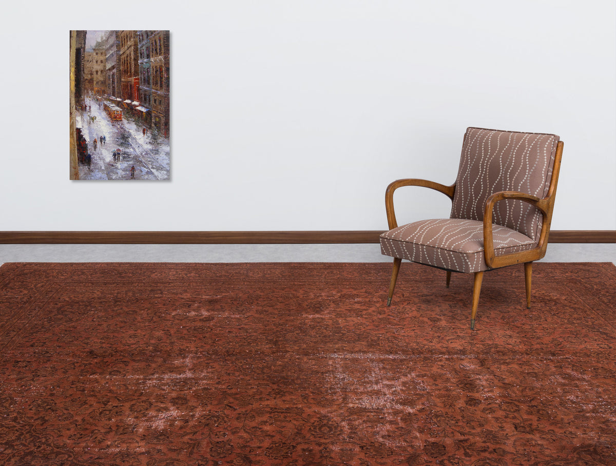 Distressed rust-red rug with a subtle traditional floral pattern, styled in a room with a patterned armchair and wall art.