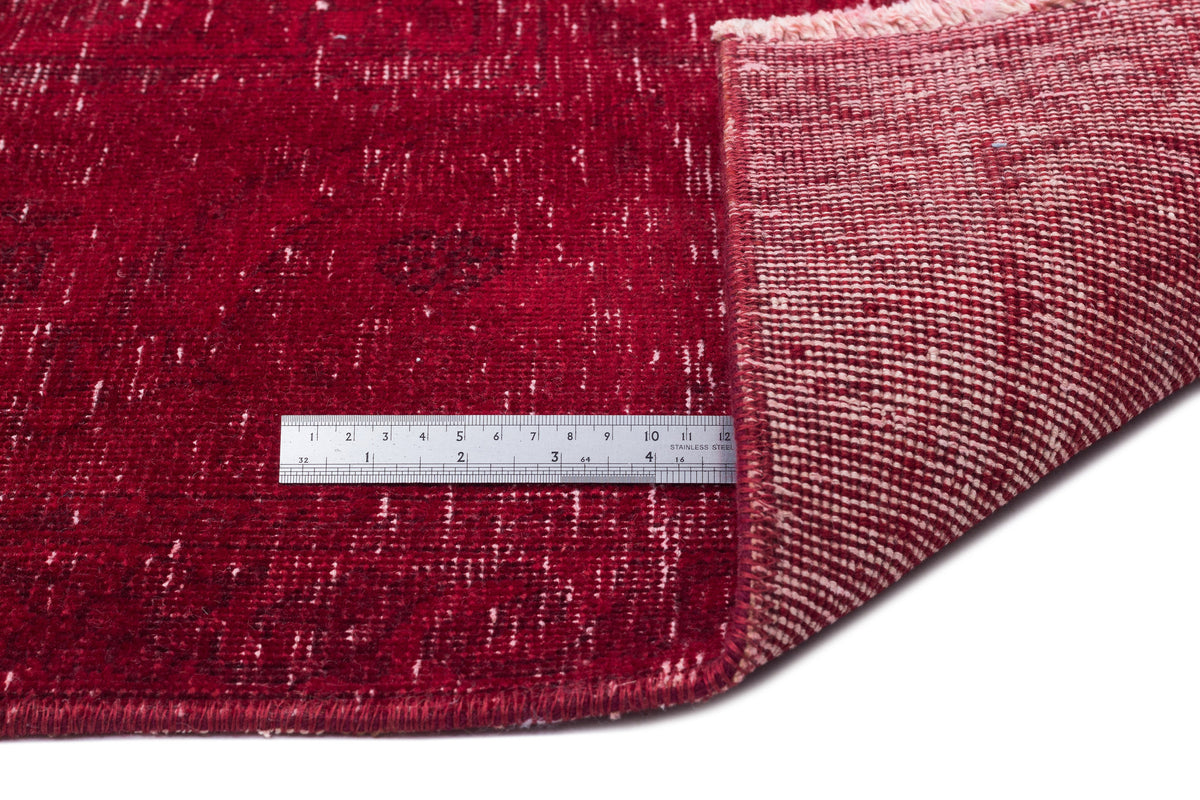 Deep red distressed rug with a visible woven backing and a stainless steel ruler for scale.