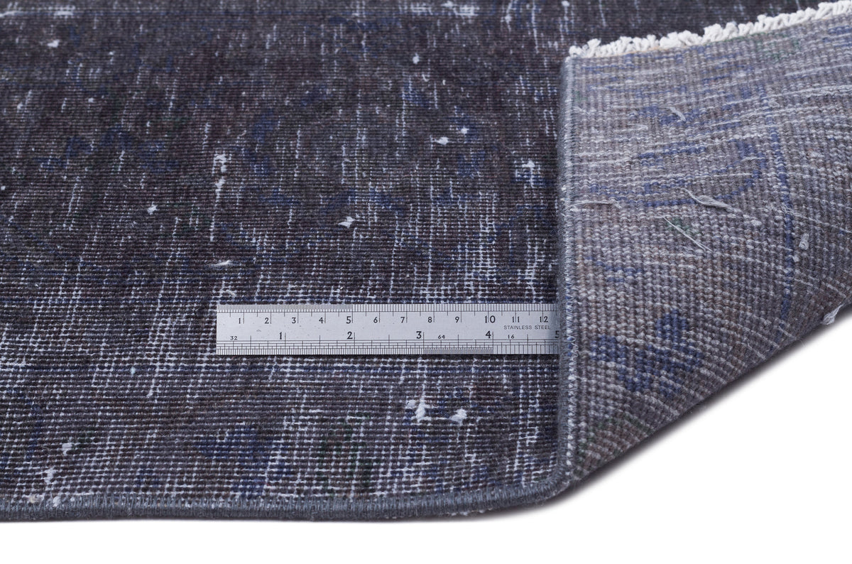 Distressed charcoal and blue rug with white flecks, showing a corner fold and a metal ruler for scale.