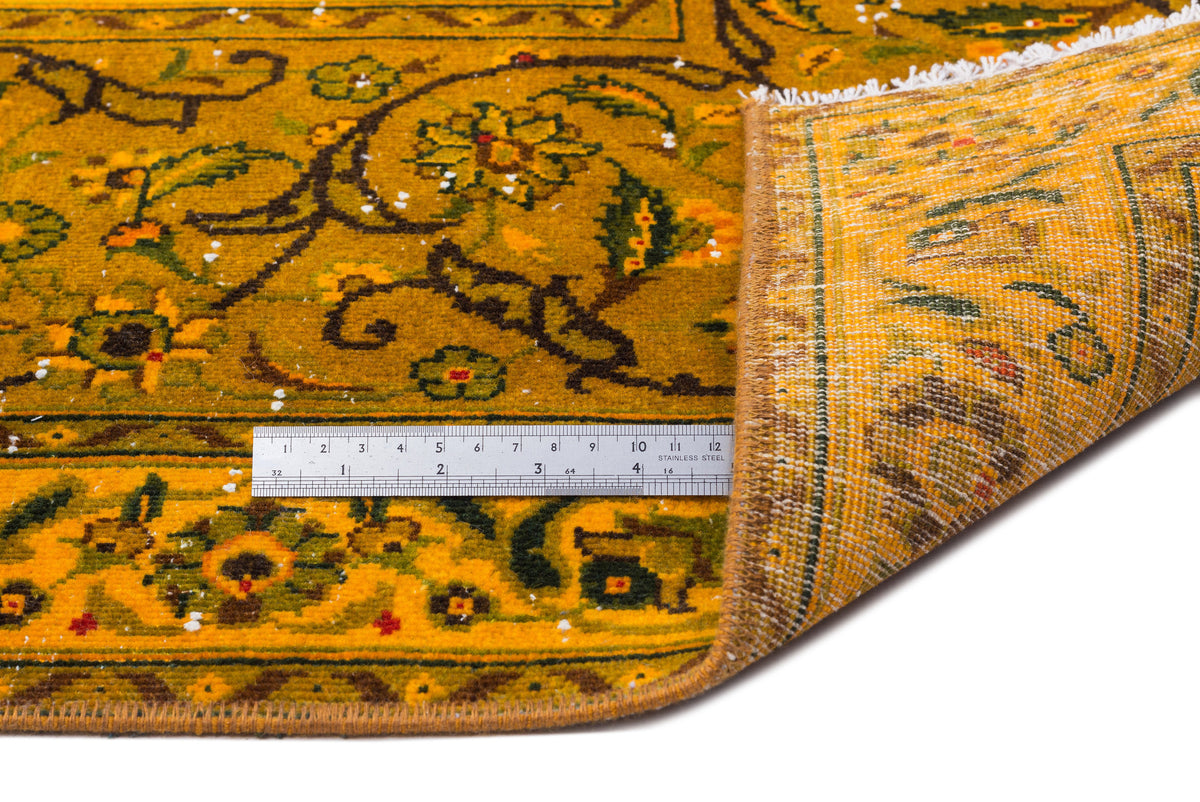 Mustard yellow rug with a dark green floral pattern and white fringe, shown with a metal ruler for scale.
