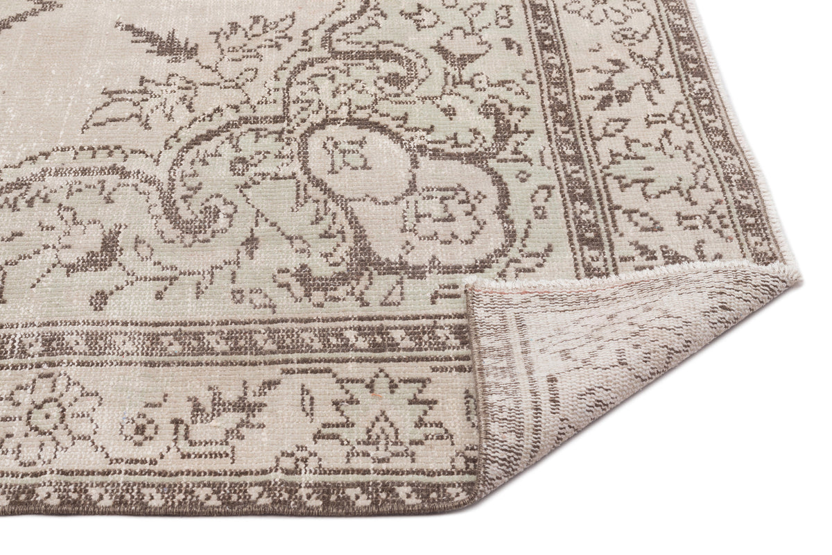 Beige and brown distressed rug with a traditional floral medallion pattern and a folded corner on a white background.