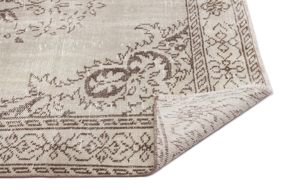 Beige and brown distressed rug with a traditional floral medallion pattern and a folded corner on a white background.
