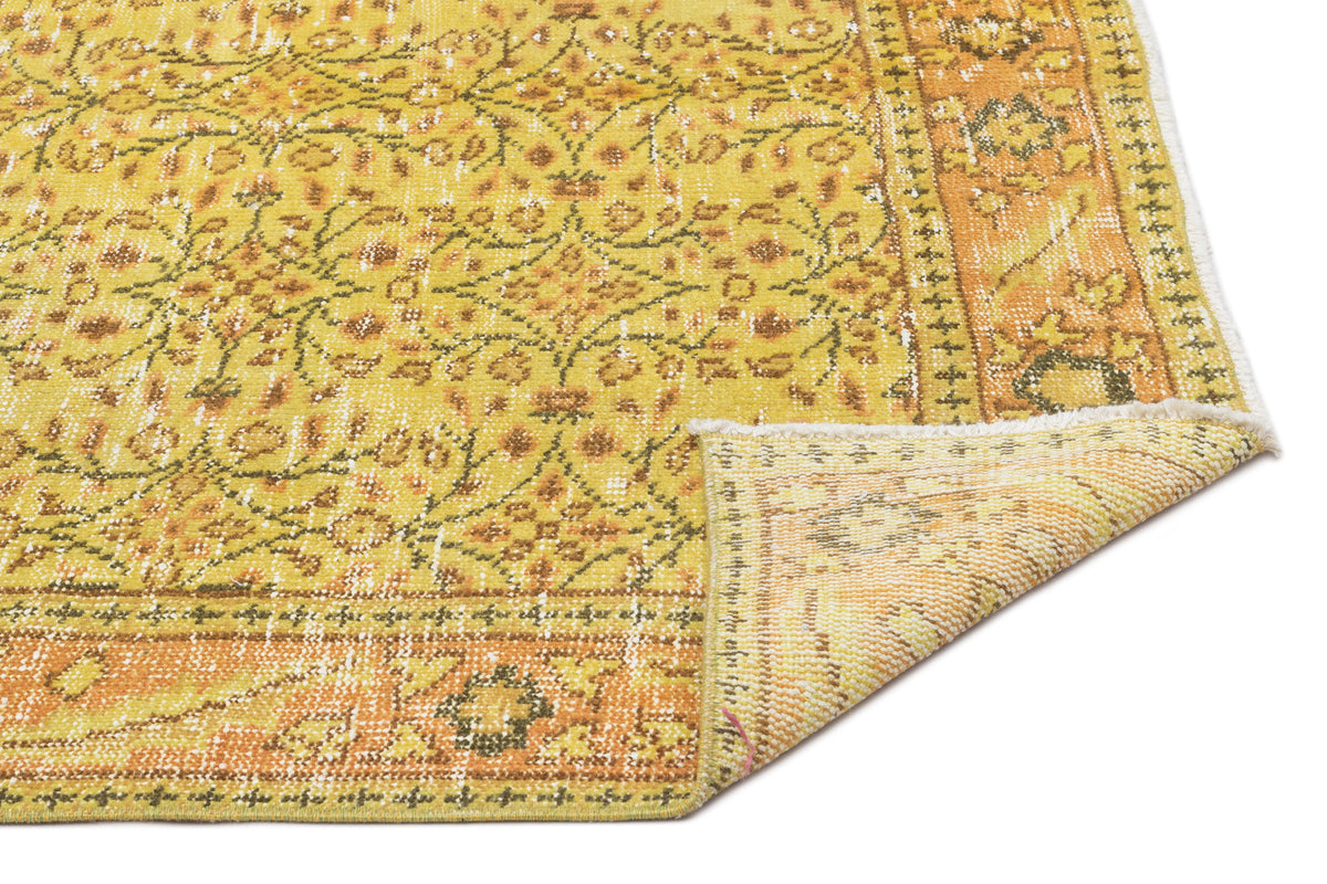 Yellow and orange distressed traditional rug with a floral medallion pattern and a folded corner showing the backing.